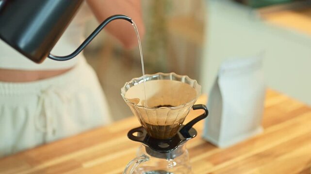 Close up of woman pouring hot water into pour over coffee dripper on a wooden kitchen counter