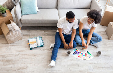 Happy African American Spouses Choosing Color Palette For Wall Painting During Renovation Sitting On Floor At Home. Interior Design Trends Concept. High-Angle View