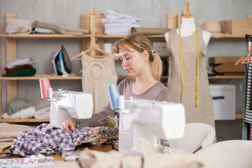 Qualified female tailor works at a sewing machine in a workshop. Dressmaker sews clothes to order for a client