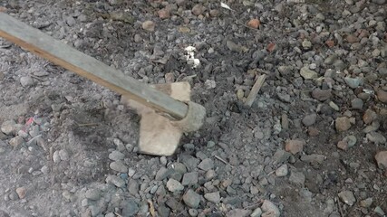 construction worker ploughing the dirt and pebbles at worksite using an old and rusty wooden hoe