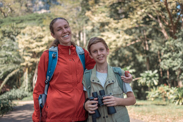 Hikers or explorers family on journey carrying backpack, trekking poles and holding binoculars looks into the distance observing guide trekking and trail exploration holiday ecotourism concept