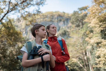 Hikers or explorers family on journey carrying backpack, trekking poles and holding binoculars looks into the distance observing guide trekking and trail exploration holiday ecotourism concept