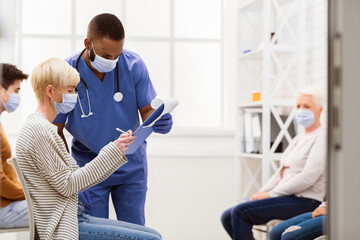 Obraz premium Patient Woman Signing Papers With Doctor Before Coronavirus Vaccination Sitting In Hospital Waiting-Room. Covid-19 Pandemic Medical Treatment Concept. Empty Space For Text