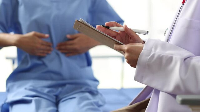 Doctor visiting patient suffering from abdominal pain in hospital room. Female physician examining and documenting abdominal pain of patient.