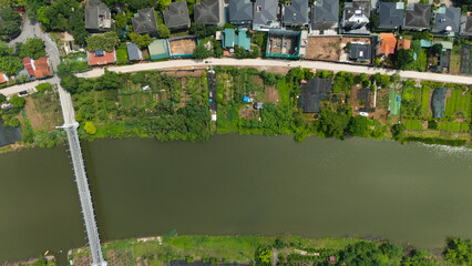 Top-down drone view of a narrow canal bordered by lush greenery and adjacent residential villas with gardens, illustrating Vietnam’s blend of waterways and suburban housing.