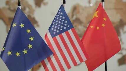 American, European Union and Chinese flags on desk with books in office on background of world map on wall in office