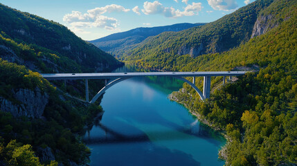Stunning view of modern bridge spanning serene river, surrounded by lush green mountains and clear blue sky