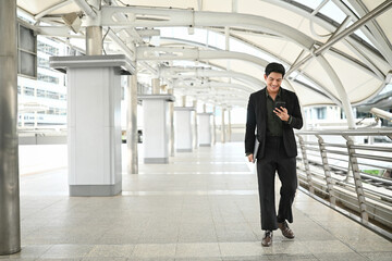 Fototapeta premium A man in a suit is walking with a cell phone in his hand and a laptop in his other hand.Concept of professionalism and busyness