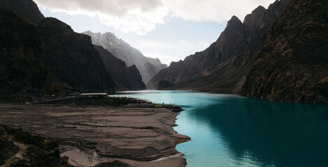 View of Attabad Lake surrounded by steep rocky mountains under a dramatic cloudy sky in Hunza Valley, Gilgit-Baltistan, Pakistan. 