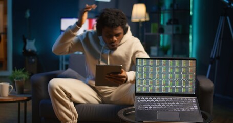 African american person using his tablet laying on the couch while he pays attention to laptop with...