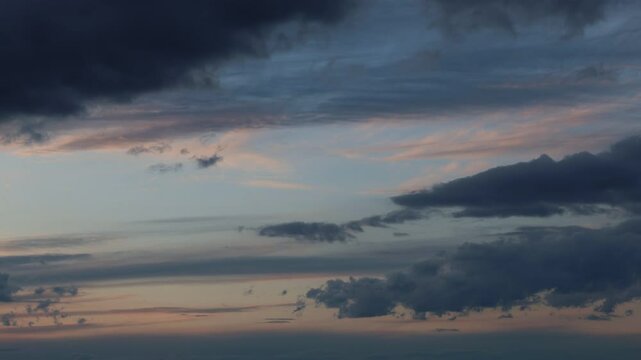 Timelapse shot of cloudy sky, flowing, billowing, moving horizontally, from left to right, blue clouds during sunset in dark color tone