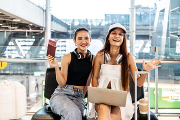 Two joyful asian female tourists eagerly await their flight at the airport, expressing excitement...