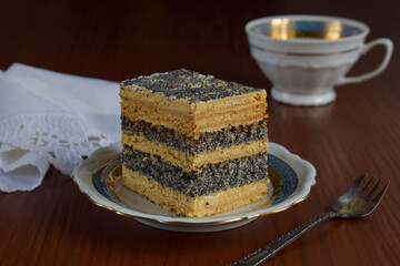Slice of traditional Ukrainian layered poppy seed cake on porcelain plate with vintage spoon. Rustic festive dessert, homemade baking, close-up food photo, Slavic cuisine, sweet pastry