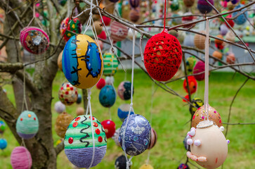 Handmade easter egg ornaments hanging from tree branches in public square. Close-up of colorful easter eggs on tree, low angle shot, joyful urban spring celebration.