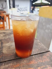 Iced tea drink in a clear plastic glass on a wooden table.