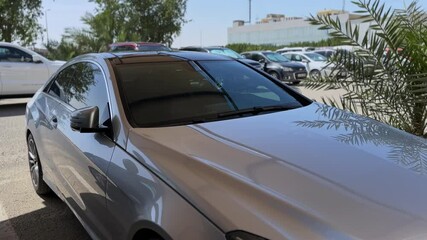 4K side view of a silver luxury car parked in sunlight with palm shadows on the hood. Perfect for automotive ads, luxury lifestyle, and car dealership visuals.