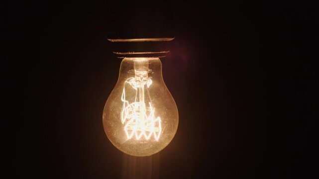 Incandescent light lamp bulb flickering on black background in dark room close-up