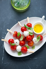 White plate with caprese skewers on a black marble background, high angle view, vertical shot, selective focus