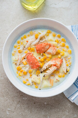Plate of corn chowder with crab meat on a beige stone background, vertical shot, high angle view