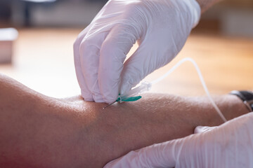 Gloved hands inserting IV needle into patient’s arm