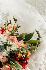 Colorful and sunny close up of a Bridal Bouquet on a white lace dress