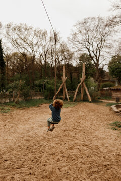 Child swinging on a long zip line in a rustic outdoor playground