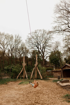 Child swinging on a long zip line in a rustic outdoor playground