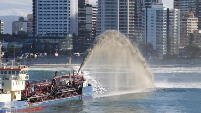 A dredger sprays sand into the ocean near Gold Coast's skyline under clear skies, enhancing beach restoration efforts