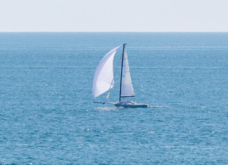 A sailboat is sailing in the ocean with a white sail