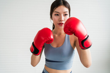 Confident young woman wearing red boxing gloves in fighting stance. Fitness and self-defense training indoors. Promotes strength, empowerment, healthy lifestyle, and female motivation.