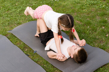 Naklejka premium Kids playing yoga outdoors on mats. Girl balances on boy.