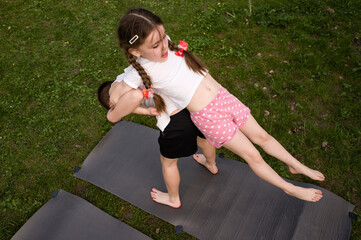 Children playing outdoors, girl lifting boy on yoga mats. Fun active playtime in the grass.