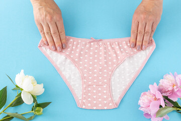Women's hands with a pink panties on the blue background.