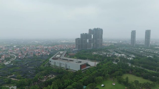 High-angle shot of a mixed urban landscape: a shopping complex roof, manicured lawns, scattered villas and clusters of tall residential blocks under bright sky