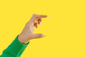 Hand gesture creating small space against bright yellow background, showcasing precision and expressiveness in body language