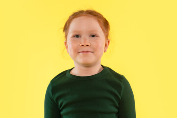 Young girl with red hair smiles against a bright yellow background showcasing her joyful...