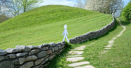 Green hill dominates landscape. Stone wall runs alongside path. Paper figure stands atop structure, idyllic scene.