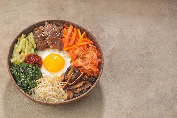 Bibimbap is a Korean dish in the form of a bowl of white rice topped with side dishes of vegetables, beef, eggs and spicy gochujang sauce.