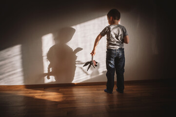 Little boy lonely depressed standing with back sitting on floor sad autism. autism spectrum disorder, psychological problems, mental health. child with a soft toy in his hands horror