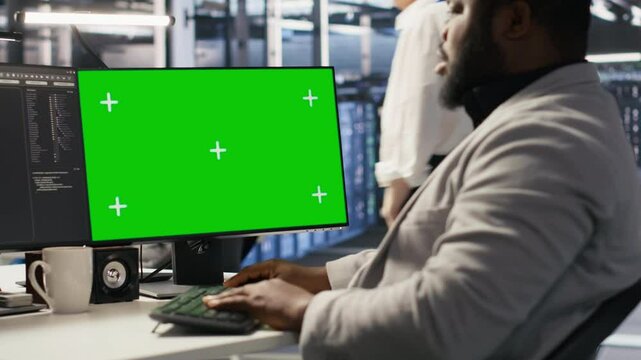 Data center programmer working on green screen desktop PC, updating storage infrastructure. IT specialist using mockup computer in server hub workspace filled with networking tech, camera A