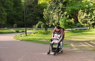 Mother walking with her baby in stroller at park. Space for text