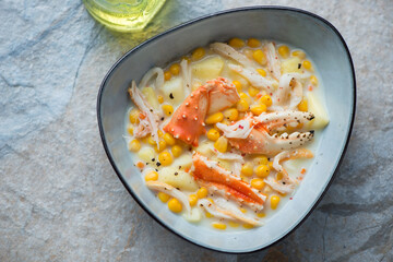 Bowl of crab and corn chowder, horizontal shot on a blue and beige stone background, high angle view