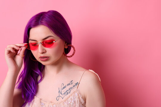 Beautiful woman with bright purple hair and tattoo in Latin on pink background. Space for text