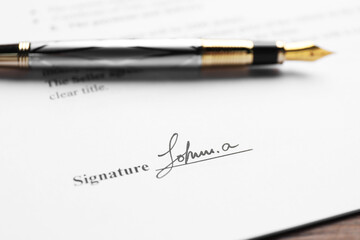 Fountain pen and signature on contract at wooden table, closeup