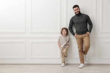 Happy father and his son near white wall indoors, space for text
