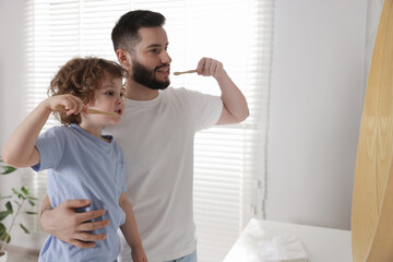 Happy father and his son brushing teeth with toothbrushes in bathroom