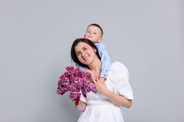Mother and her son with bouquet of lilac flowers on light grey background