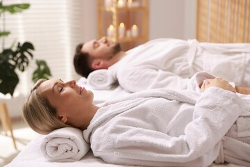 Couple in bathrobes lying on massage tables in spa salon, selective focus