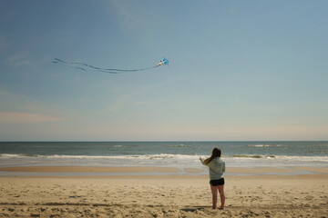 Behind teen girl flying colorful kite on beach Cape Hatteras Nat