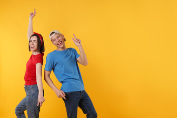 Obraz premium Happy couple in stylish clothes dancing on yellow background. Space for text